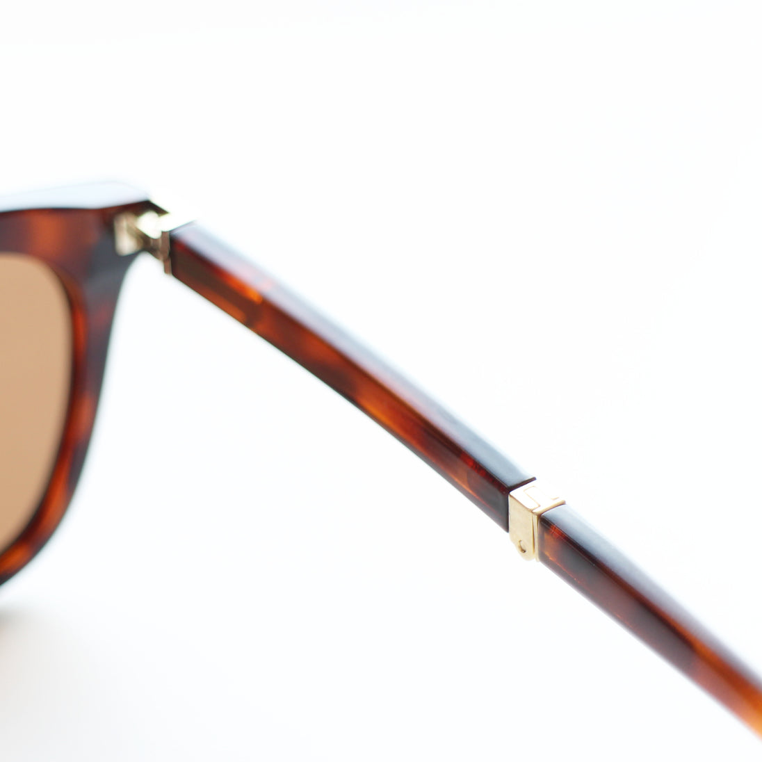 Close-up of a tortoiseshell folding sunglasses frame with a gold accent on a white background