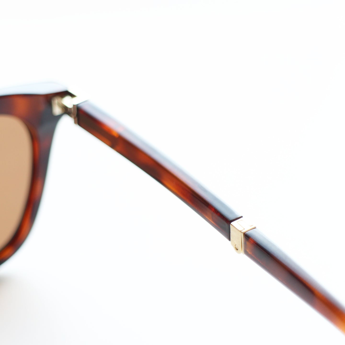 Close-up of a tortoiseshell folding sunglasses frame with a gold accent on a white background